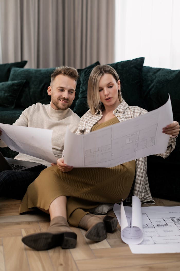 A couple sitting on the floor, examining house blueprints in a cozy home setting.